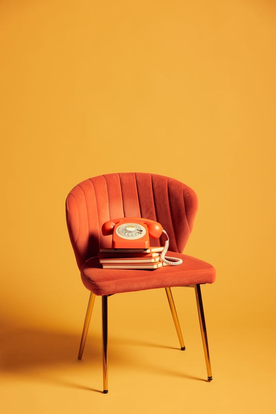 An orange rotary telephone on a stack of three orange notebooks, sitting on an orange chair.